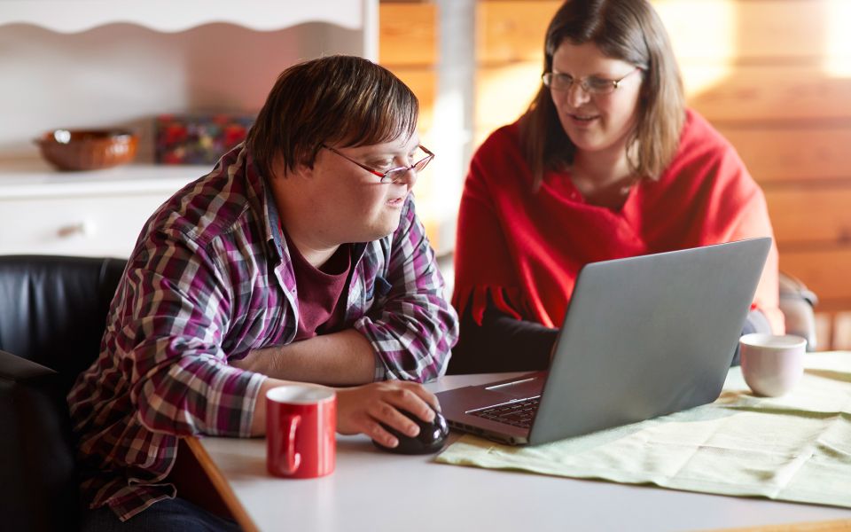 Eine behinderte Person arbeitet mit einer weiteren Person an einem Computer.