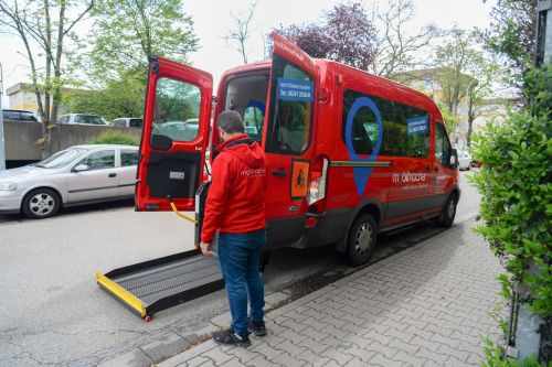 Das Bild zeigt ein rotes Fahrzeug des Fahrdienstes „Mobilmacher“, dessen Rampe ausgeklappt ist und von einem Mitarbeiter bedient wird.